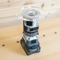 Clear 6-inch round acrylic router base plate mounted on an upside-down Flex 24V trim router on a workbench