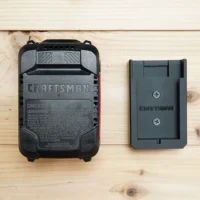 Black plastic battery mount for Craftsman 20v battery shown next to a Craftsman battery on light wood surface
