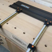 Black parallel guide brackets with orange knurled screws mounting Incra T-Track rails to a Ridgid guide rail on a Sjobergs bench