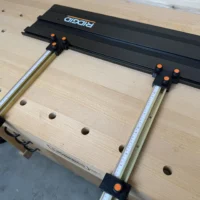 ToolCurve Parallel Guides mounted on Ridgid track saw rails, with black brackets and orange knobs securing dual aluminum guide bars over a workbench with pocket holes