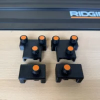 Black plastic parallel guide brackets with orange adjustment knobs, displayed in two rows next to a Ridgid track saw rail
