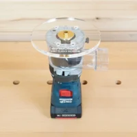 6-inch round clear acrylic base plate attached to a Bosch Colt 18V trim router, mounted on a wood workbench