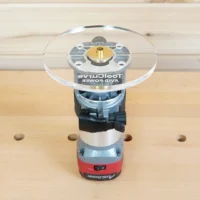 Clear acrylic 6-inch round router base plate mounted on an Avid Power trim router, showing the brass center bushing and mounting hardware from above