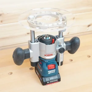 Clear 8-inch round acrylic router base plate mounted on an inverted Bosch Colt plunge router base, center bushing opening visible