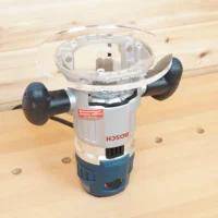8-inch clear acrylic router base plate mounted on a Bosch MR23EVS plunge router, showing the large round base and factory tool heads