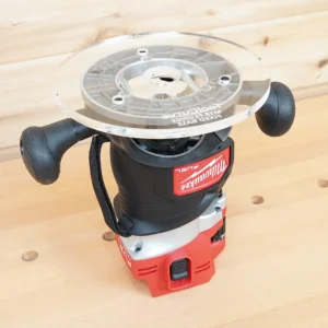 Clear 8-inch round acrylic router base plate mounted upside down on a Milwaukee M18 Fuel router