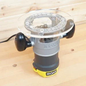 Clear 8-inch round acrylic router base plate mounted on an upside-down Ryobi plunge router on a wood bench