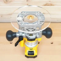 8-inch clear acrylic router base plate attached to a Dewalt DNP612 plunge router, showing brass center post and guide bushing opening from above