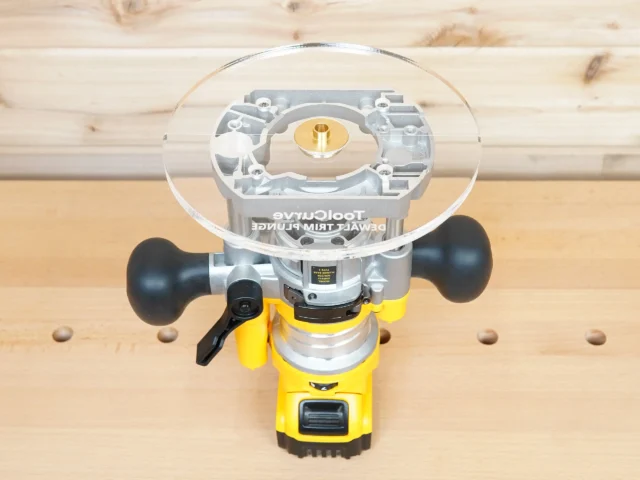 8-inch clear acrylic router base plate attached to a Dewalt DNP612 plunge router, showing brass center post and guide bushing opening from above