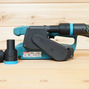 Black 27mm hose adapter with blue collar installed on a Makita 9910 belt sander, second adapter beside it