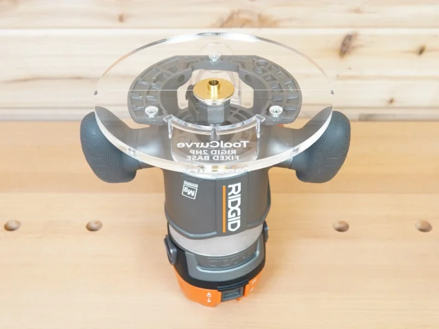 8-inch clear acrylic router base plate mounted on a Ridgid 2 HP fixed base router, viewed from above on a wood workbench