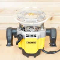 DeWalt plunge router with yellow housing and black handles, fitted with clear acrylic 8-inch round base plate, viewed from above on wooden workbench
