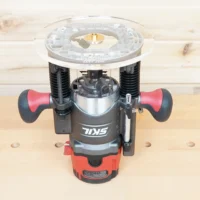 Clear acrylic router base plate mounted on a Skil RT1322 plunge router, showing the 8-inch round base from above with brass threaded insert at center